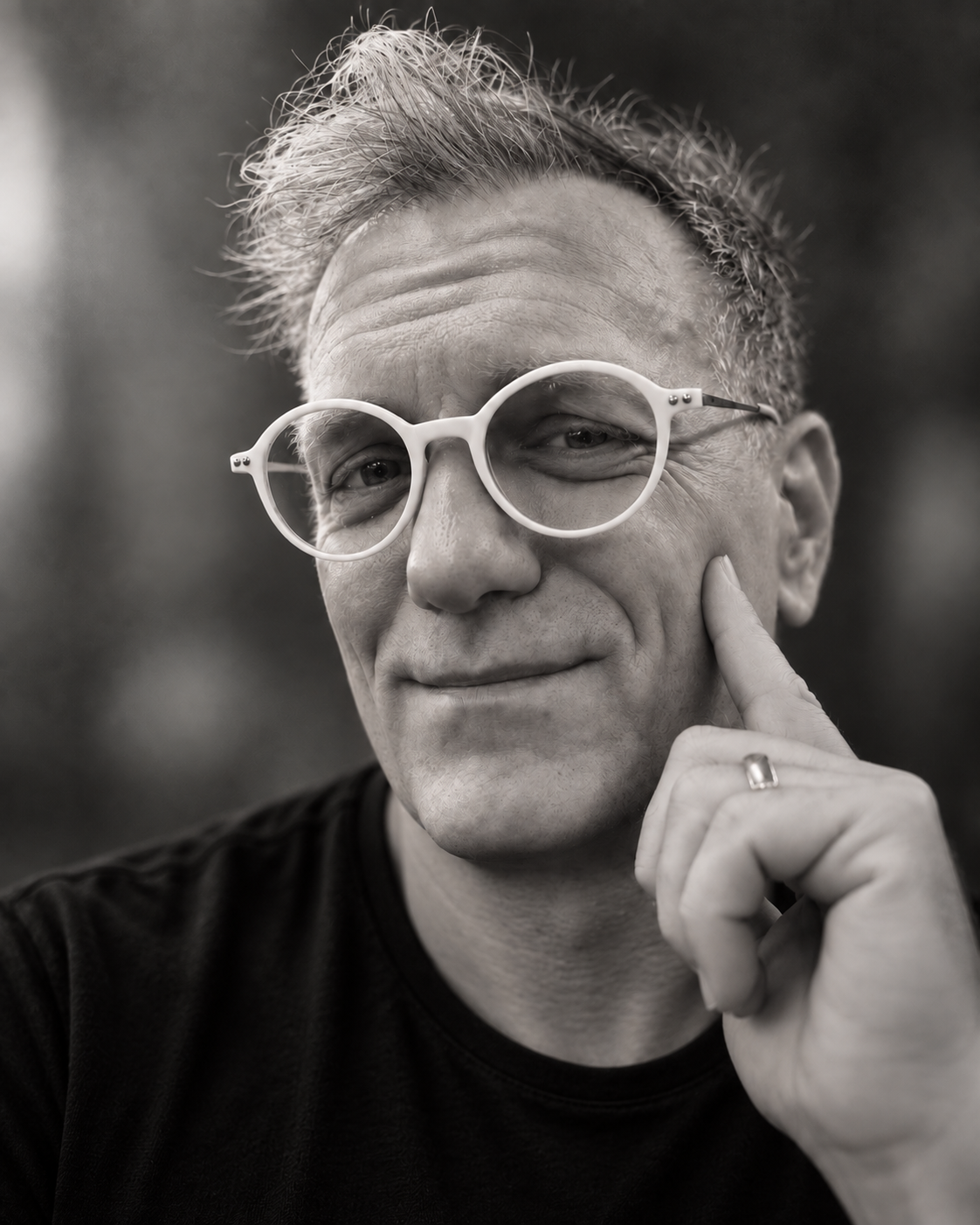 Steven Ochs wearing white glasses and a black T-shirt, resting a finger against his cheek